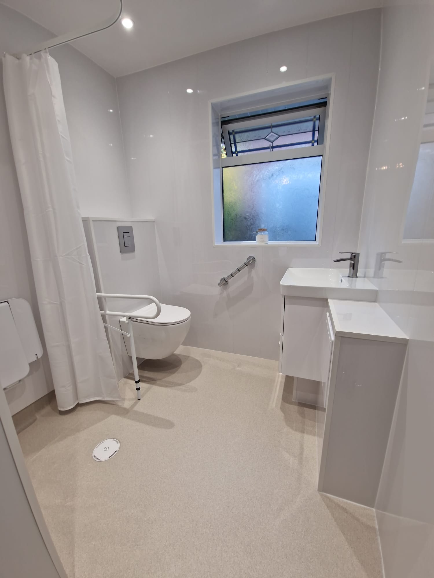 Wall-hung toilet with support rail beside a basin in the completed wet room